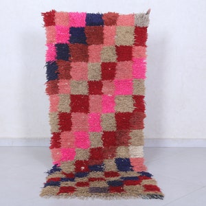 May include: A pink, red, brown and blue checkered rug with a shaggy texture. The rug is made of wool and is perfect for adding a touch of colour and texture to any room.