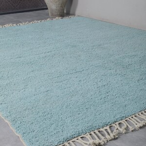 May include: A light blue rug with a fringe border. The rug is made of a soft, fluffy material.