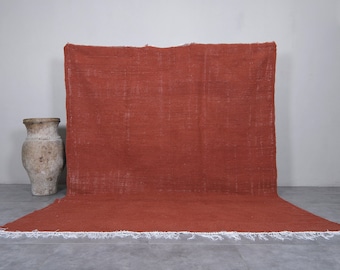 May include: A large, rectangular, rust-colored rug with a white fringe border. The rug is lying flat on a gray floor.