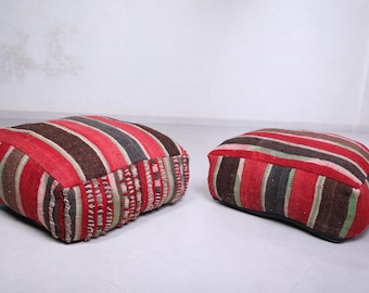 May include: Two red, brown, and green striped floor cushions. The cushions are square and have a fringe around the edges.