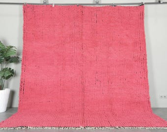 Op de afbeelding: Een groot, rechthoekig, roze tapijt met een getextureerd oppervlak. Het tapijt hangt aan een metalen stang. Het tapijt heeft een franje langs de onderrand. Het tapijt is gemaakt van een dik, geweven materiaal.
