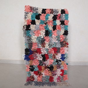 Puede incluir: Una alfombra colorida tejida a mano con un patr&oacute;n a cuadros en tonos de rosa, azul, gris y negro. La alfombra tiene un borde de flecos y est&aacute; hecha de materiales reciclados.