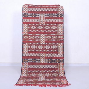 May include: A red, white, and black patterned rug with geometric designs. The rug has a fringe on the bottom.