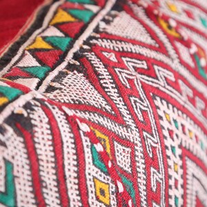 May include: Close-up of a red, white, green, and black patterned fabric with a geometric design. The fabric is woven and has a textured surface.