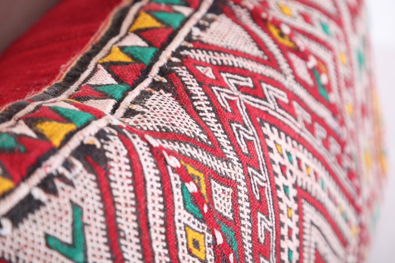 May include: Close-up of a red, white, green, and black patterned fabric with a geometric design. The fabric is woven and has a textured surface.