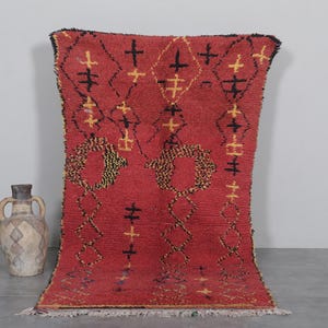 May include: A red Moroccan rug with a geometric pattern in black and yellow. The rug has a fringe border.
