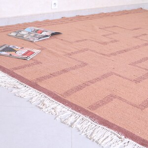 May include: A light brown rug with a geometric pattern in a darker brown colour. The rug has white fringe around the edges.