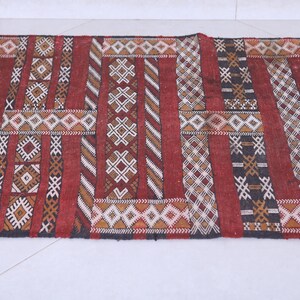 May include: A red, black, and white patterned rug with geometric designs. The rug is woven with a variety of textures and colors.