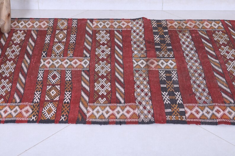 May include: A red, black, and white patterned rug with geometric designs. The rug is woven with a variety of textures and colors.