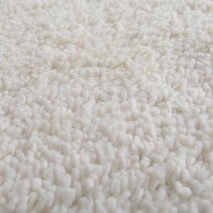 Op de afbeelding: Close-up van een witte, pluche badmat. De mat heeft een zacht, getextureerd oppervlak.