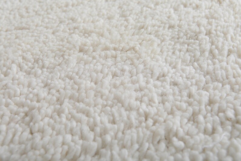 Op de afbeelding: Close-up van een witte, pluche badmat. De mat heeft een zacht, getextureerd oppervlak.