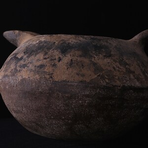 May include: A large, brown, earthenware jug with a wide, rounded body and a single handle. The jug has a rough, textured surface and appears to be very old.