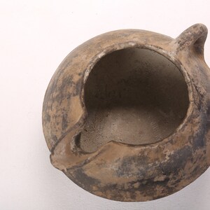 May include: A brown clay pot with a single handle. The pot has a wide opening and is slightly chipped on the rim.