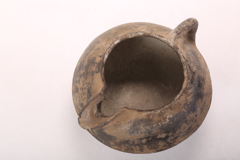 May include: A brown clay pot with a single handle. The pot has a wide opening and is slightly chipped on the rim.