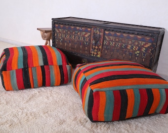 May include: Two colorful striped floor cushions with a dark wood chest with intricate painted designs in the background.