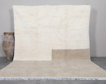 May include: A white and beige handwoven rug with a geometric design. The rug has a fringe border.