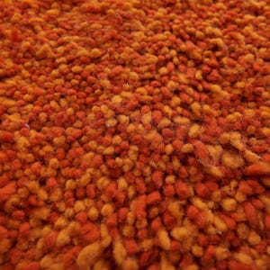May include: Close-up of a textured orange and brown rug. The rug is made of short, fuzzy fibers that create a soft and inviting look.