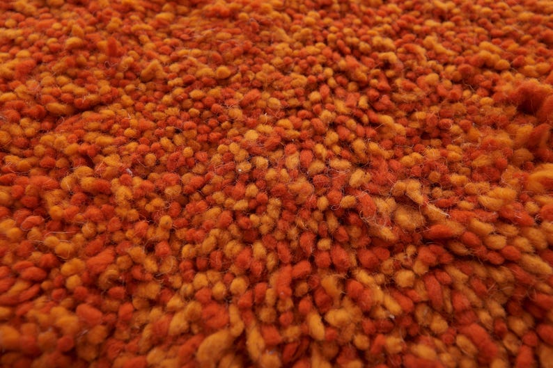 May include: Close-up of a textured orange and brown rug. The rug is made of short, fuzzy fibers that create a soft and inviting look.