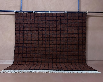 May include: A brown and black checkered rug with a textured surface. The rug has a grid pattern and a white fringe along the bottom edge. The rug is hanging from a black bar.