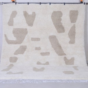 May include: A white rug with a beige abstract pattern. The rug has a fringe border.