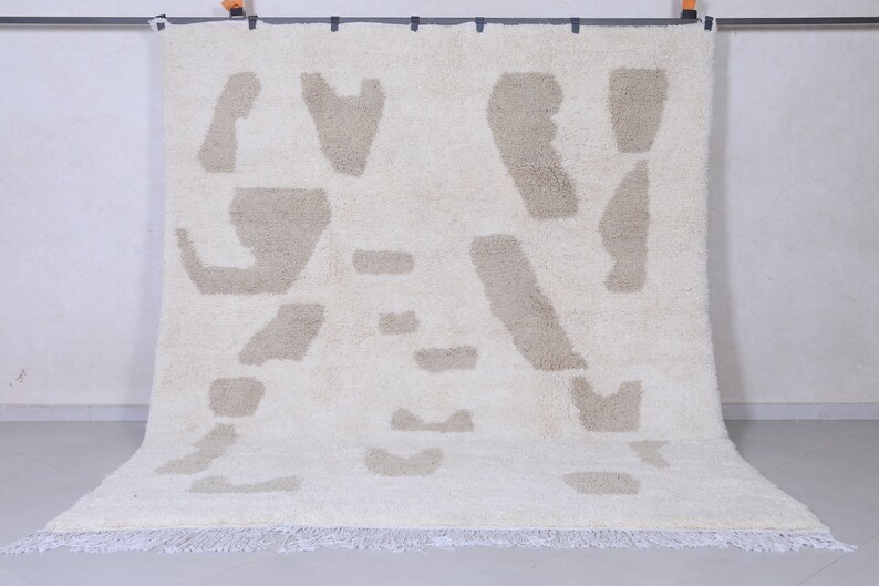 May include: A white rug with a beige abstract pattern. The rug has a fringe border.
