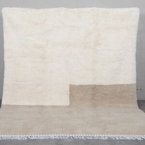 Puede incluir: Una alfombra tejida a mano de color blanco y beige con un dise&ntilde;o geom&eacute;trico. La alfombra tiene un borde de flecos.