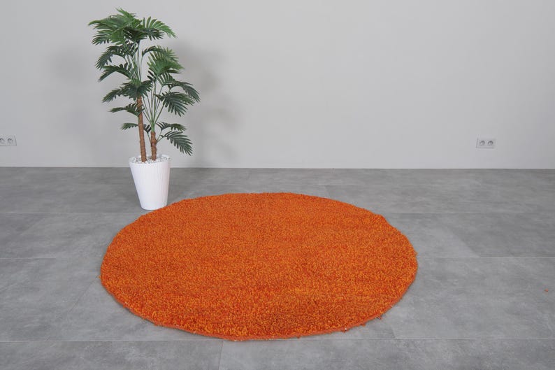 May include: A round, orange shag rug on a gray tiled floor.
