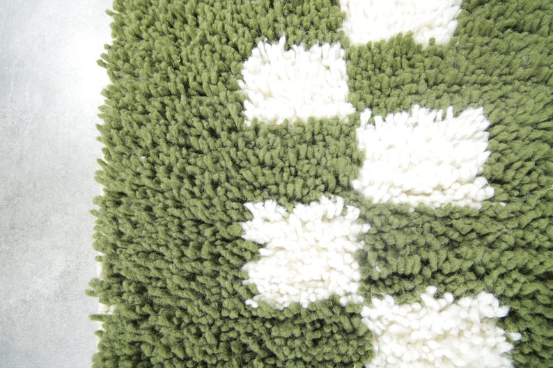 May include: Close-up of a green and white shag rug. The rug has a textured, plush appearance with a pattern of white, square-shaped accents against a green background. The rug's design is simple and modern.