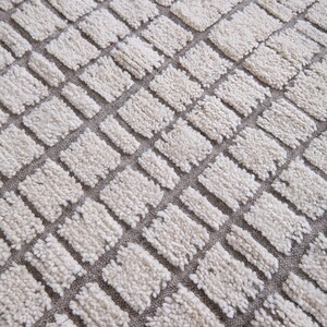 May include: A white and gray round rug with a geometric pattern of squares. The rug is made of a soft, fluffy material.