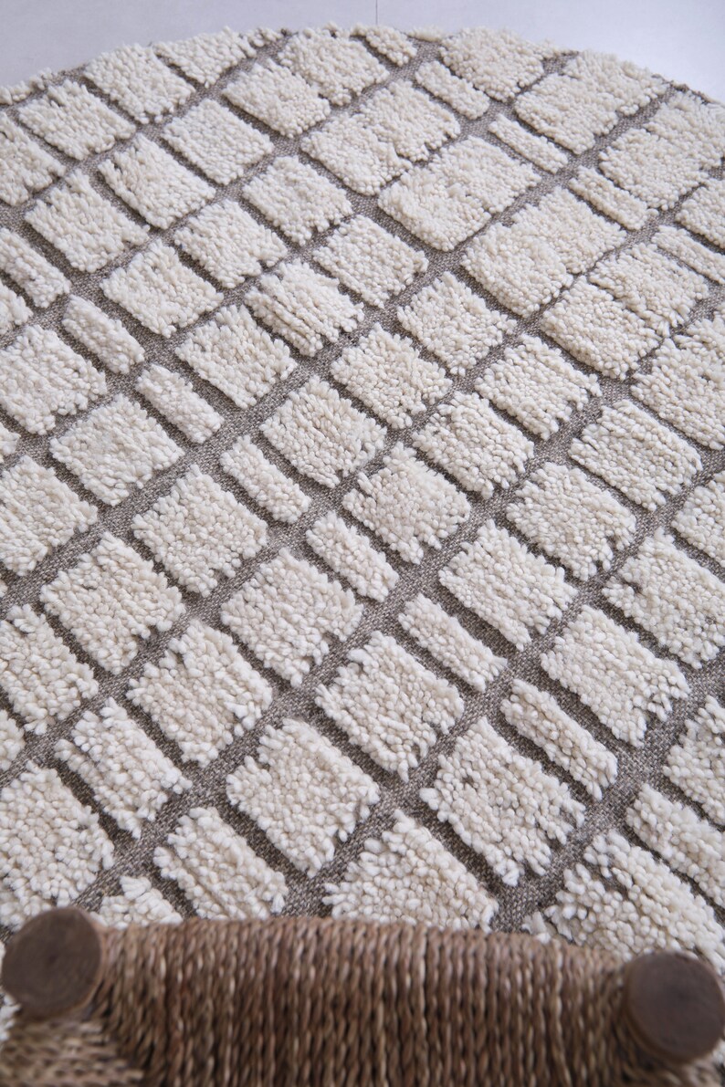 May include: A white and gray round rug with a geometric pattern of squares. The rug is made of a soft, fluffy material.