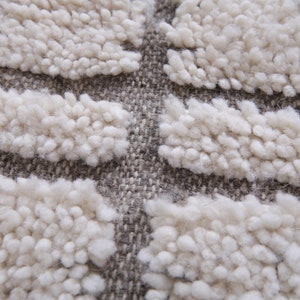 May include: Close-up of a beige and gray textured rug with a raised pattern. The rug has a woven look and feel.