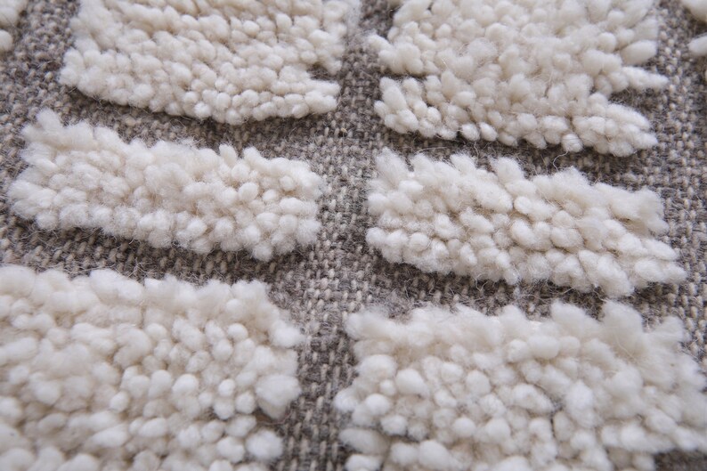 May include: Close-up of a beige and gray textured rug with a raised pattern. The rug has a woven look and feel.