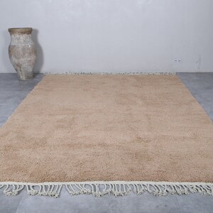 May include: A beige shag rug with a white fringe border. The rug is laid out on a gray tiled floor.