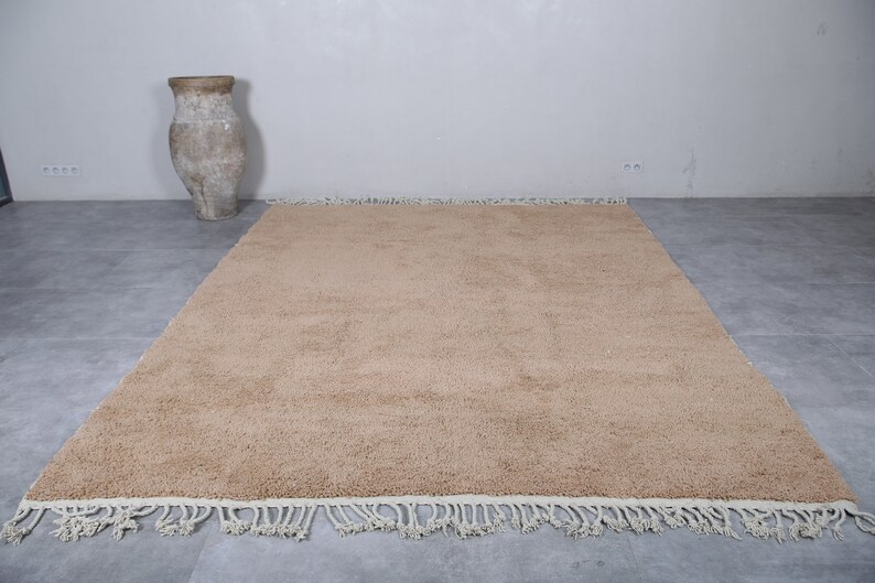 May include: A beige shag rug with a white fringe border. The rug is laid out on a gray tiled floor.