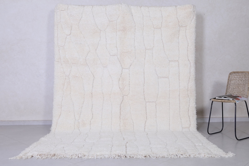 May include: A white shag rug with a unique, abstract pattern. The rug has a fringe border and is made of soft, fluffy fibres.