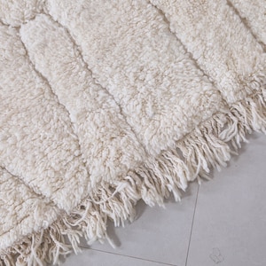May include: A white, fluffy rug with a geometric pattern and fringe along the edges.
