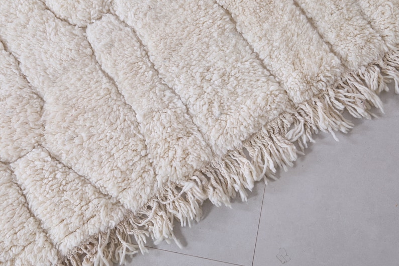 May include: A white, fluffy rug with a geometric pattern and fringe along the edges.