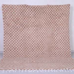 May include: A beige and white checkered rug with a fringe border. The rug is made of a soft, woven material.