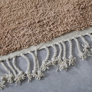 May include: A brown shag rug with a white fringe border. The rug is made of soft, fluffy fibers and has a simple, modern design.
