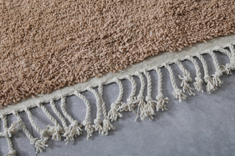 May include: A brown shag rug with a white fringe border. The rug is made of soft, fluffy fibers and has a simple, modern design.