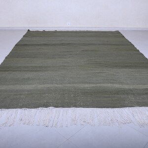 May include: A green woven rug with a white fringe. The rug has a subtle striped pattern.