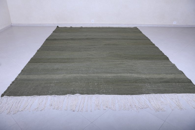 May include: A green woven rug with a white fringe. The rug has a subtle striped pattern.