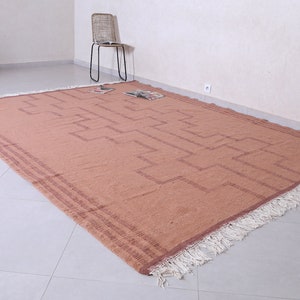 May include: A large, rectangular, rust-coloured rug with a geometric pattern and white fringe. The rug is laid out on a light grey tiled floor.