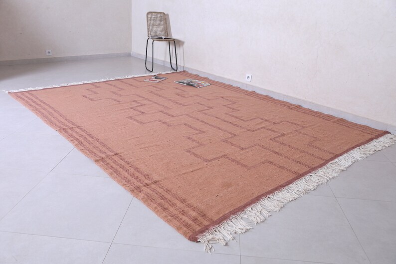 May include: A large, rectangular, rust-coloured rug with a geometric pattern and white fringe. The rug is laid out on a light grey tiled floor.