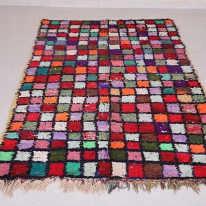 May include: A colorful Moroccan rug with a geometric pattern of squares in various shades of red, orange, green, blue, purple, and white. The rug has a fringe border.
