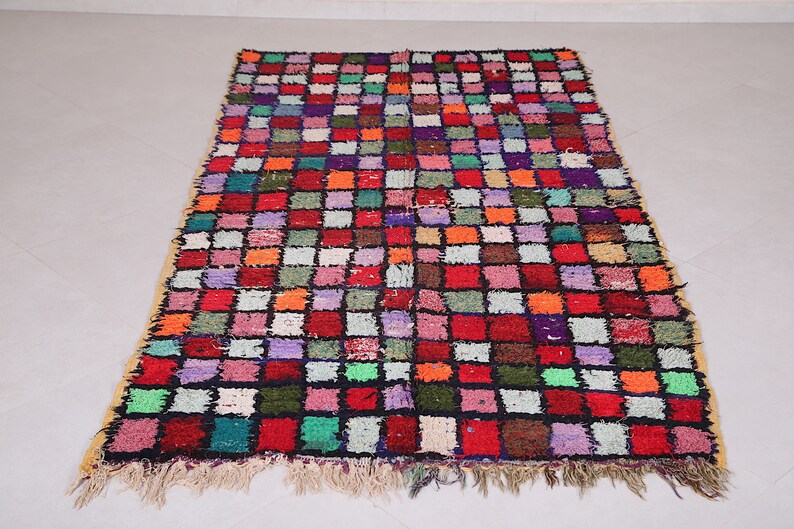 May include: A colorful Moroccan rug with a geometric pattern of squares in various shades of red, orange, green, blue, purple, and white. The rug has a fringe border.