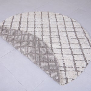 May include: A round, cream-colored rug with a geometric pattern. The rug is folded in half, revealing a beige underside with a similar pattern.