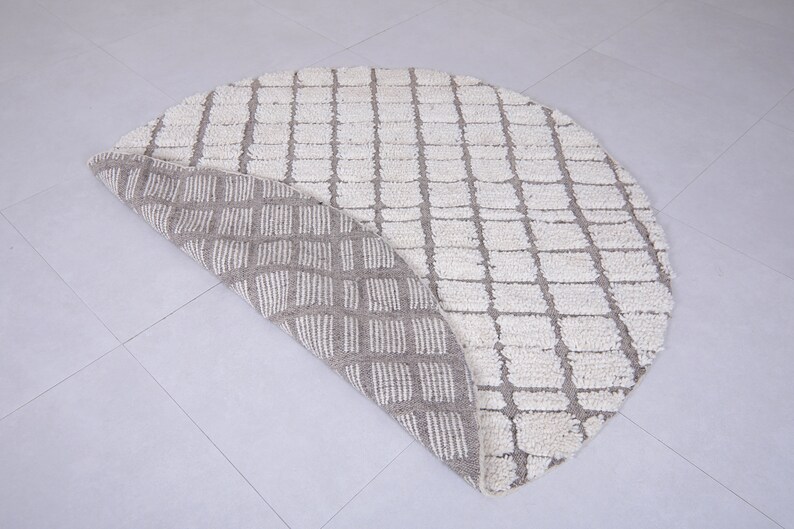 May include: A round, cream-colored rug with a geometric pattern. The rug is folded in half, revealing a beige underside with a similar pattern.