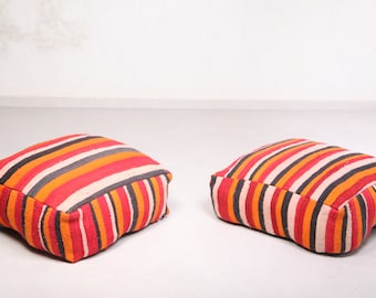May include: Two striped floor cushions in red, orange, black, white, and gray. The cushions are made of woven fabric and have a square shape.