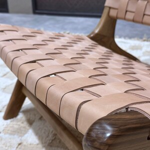 May include: A close-up of a woven leather chair seat. The seat is made of light brown leather straps woven together in a grid pattern. The chair frame is made of dark wood.